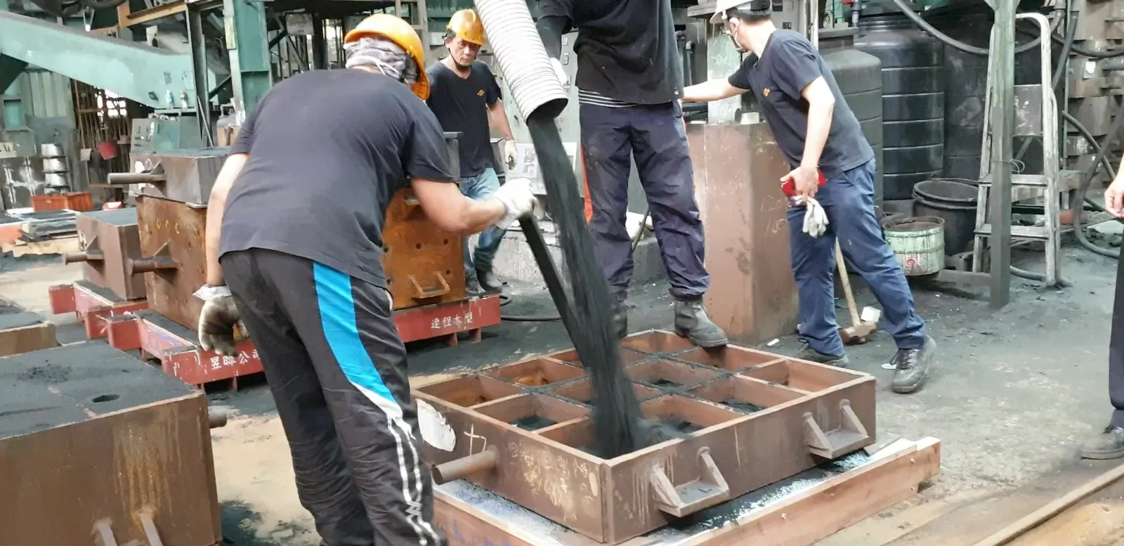 鑄造現場，工人在砂箱裡填砂